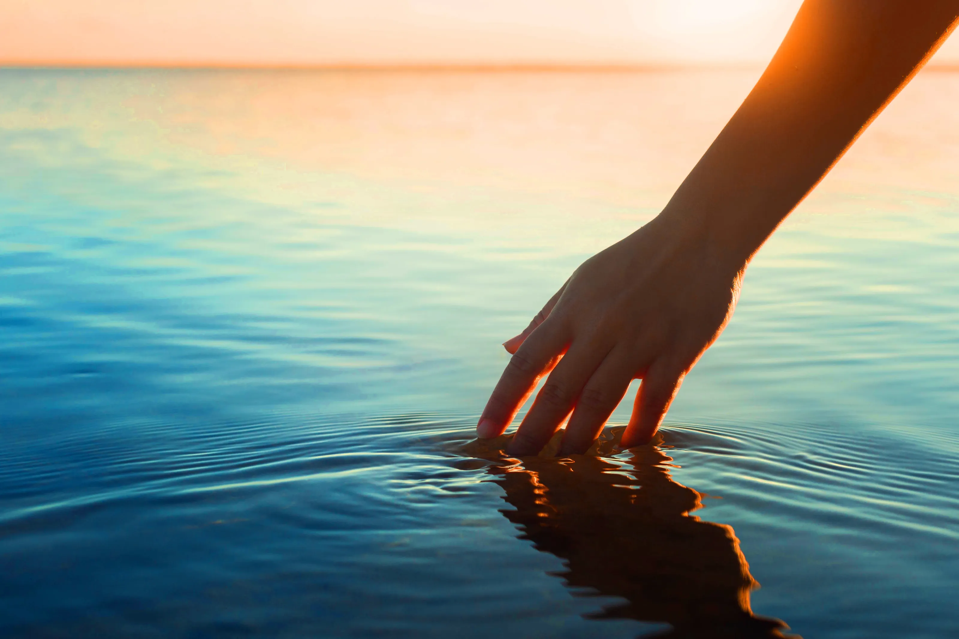 Hintergundbild: Hand durchstreift Meereswasser im Abendrot